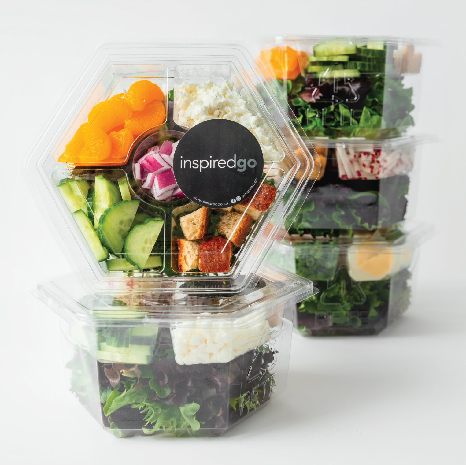 Stacked Inspired Go salad containers featuring fresh vegetables and high-quality ingredients in clear hexagonal packaging.